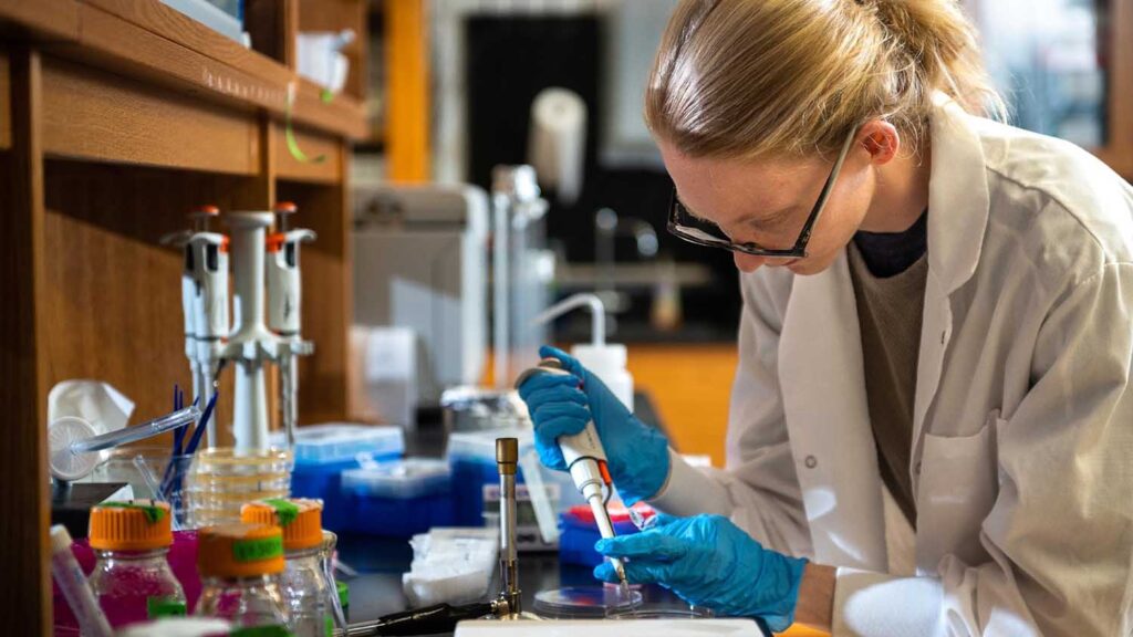 a woman with glasses uses a pipette in a lab