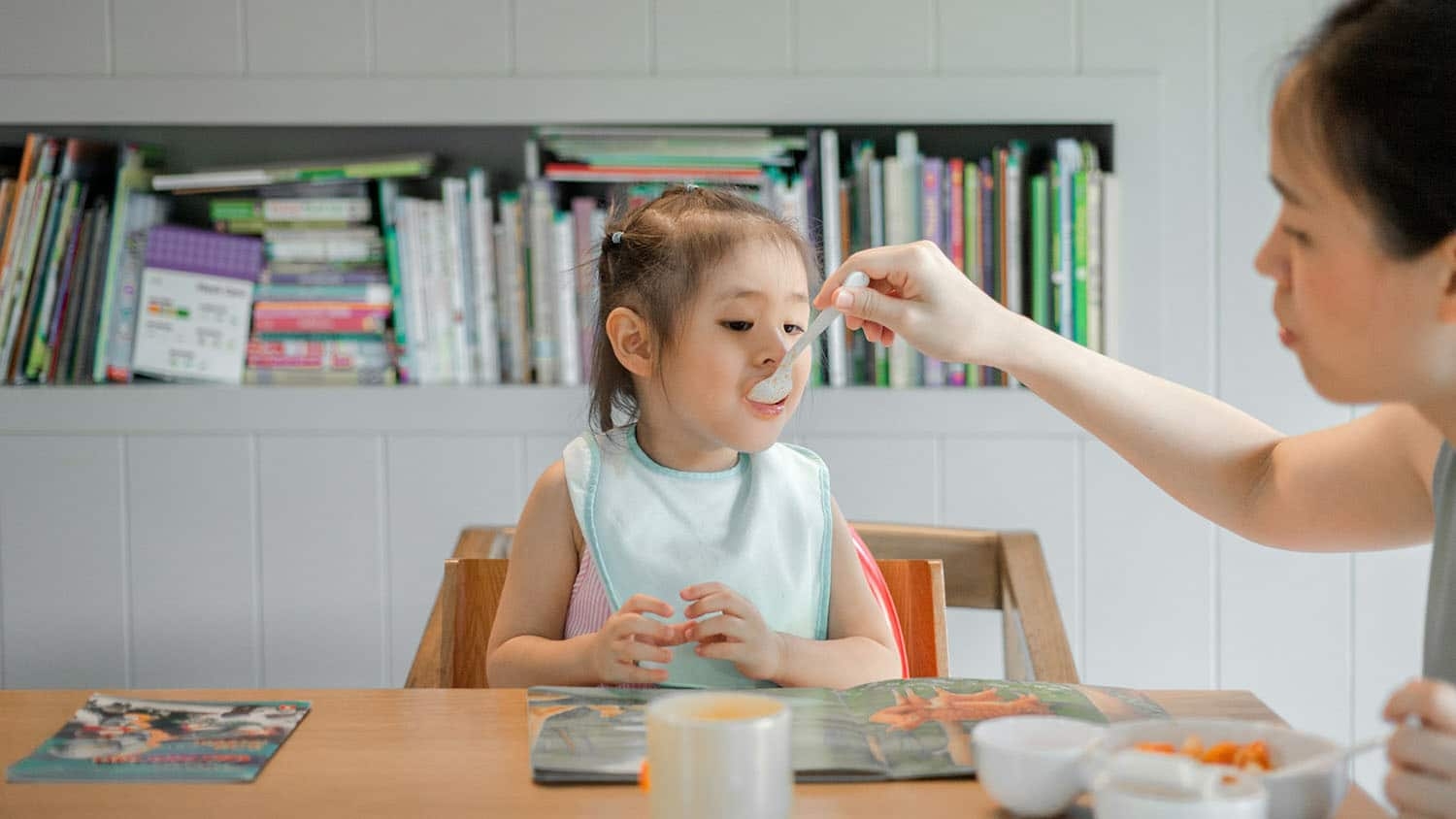a woman feeds a toddler with a spoon