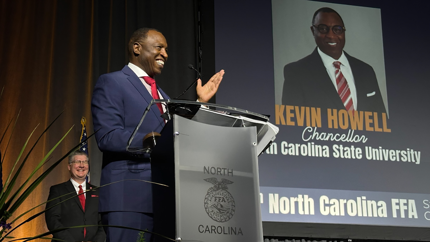 a man wearing a blue suit and red tie stands at a podium that says North Carolina with the FFA emblem in the center