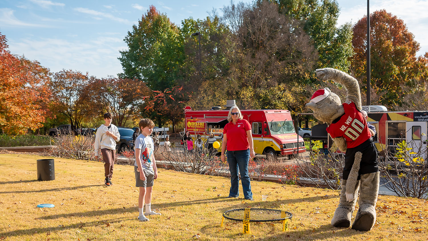 two boys and a mom play spike ball with Mr. Wuf on a lawn outside of the Plant Sciences Building at NC State