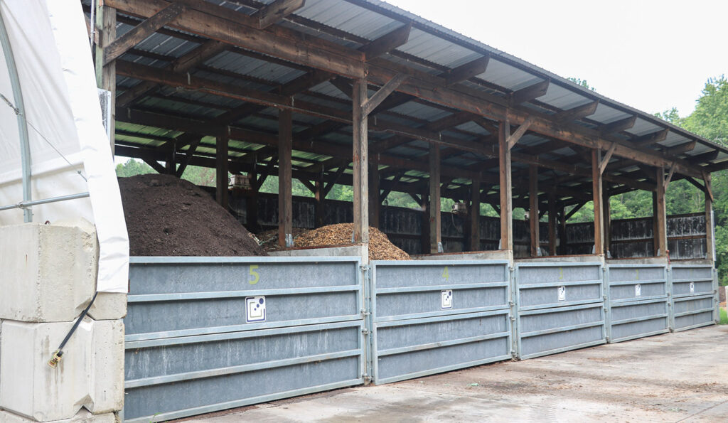 a pole barn with a sheetmetal roof with different piles of brown compost under neath the roof