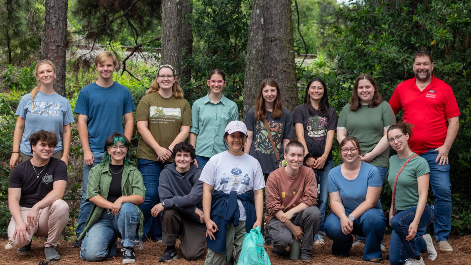 15 people pose in front of trees and bushes for a group photo