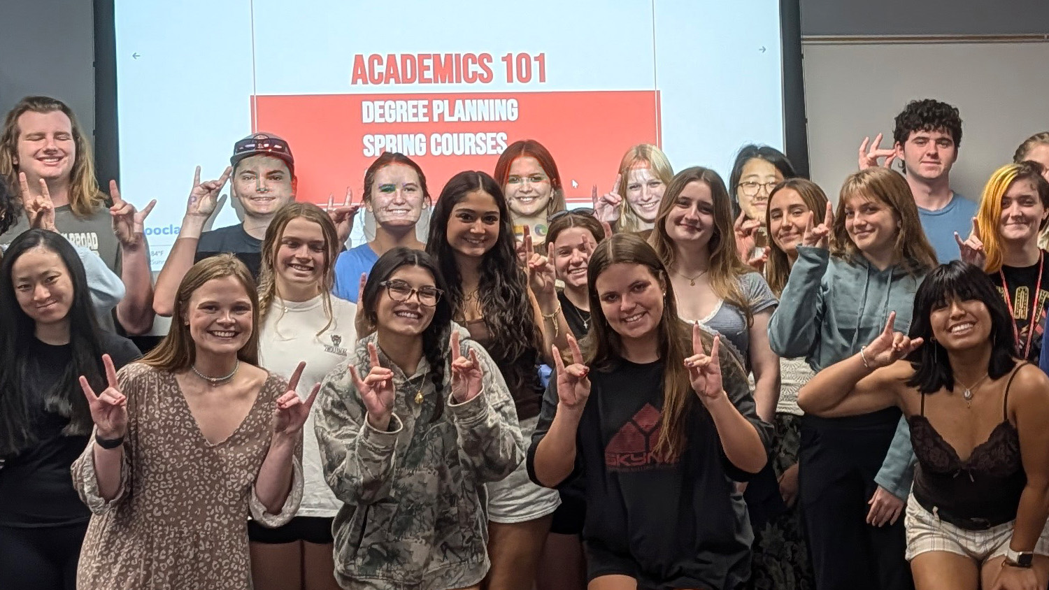 a large group of people making wolfy ears with their hands standing in front of a projector screen that says academics 101 degree planning spring courses