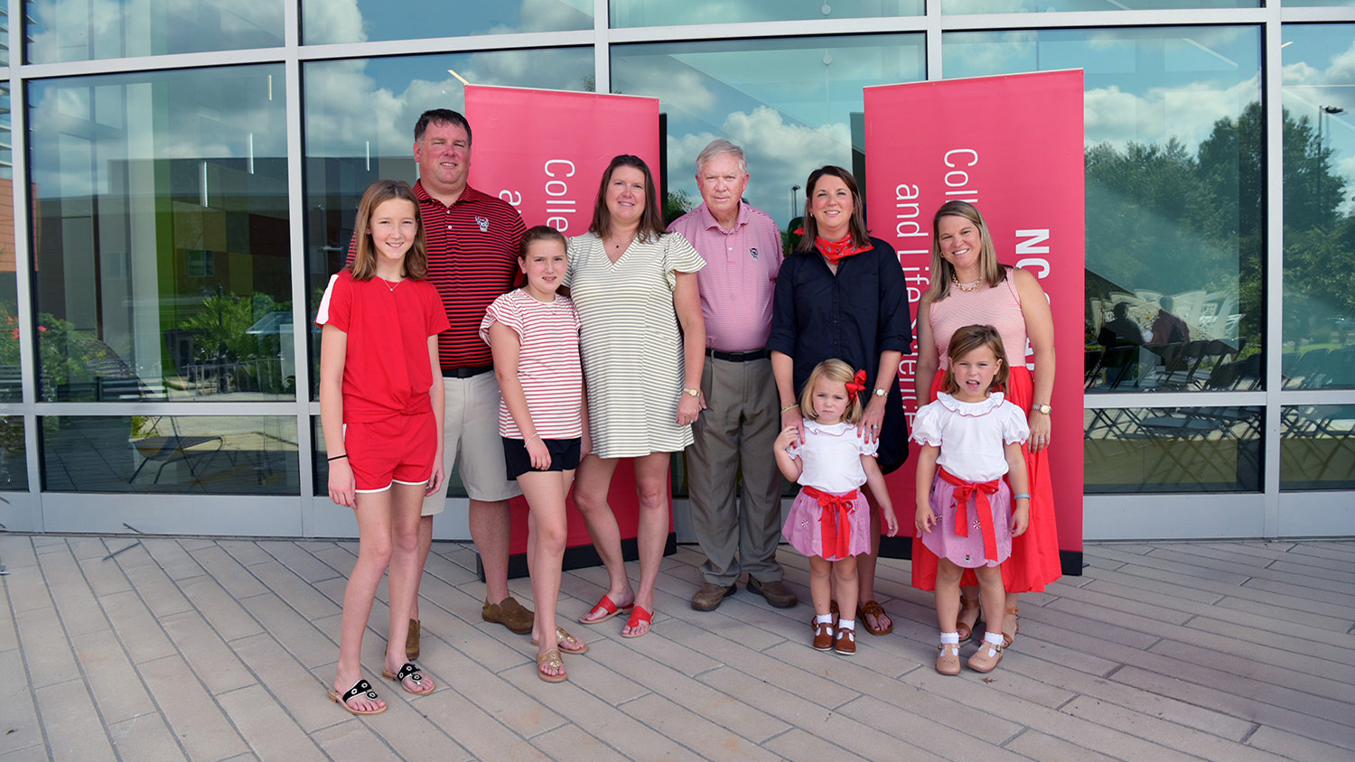 nine people including four children stand in front of a building with red signs that say nc state university college of agriculture and life sciences