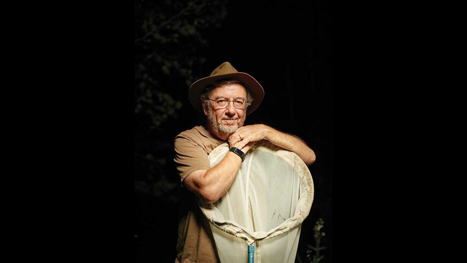 a man stands with a butterfly net in the dark