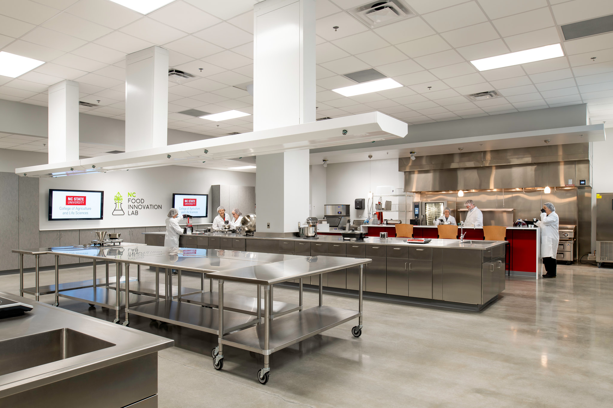 a large industrial kitchen lab with white walls, silver tables and a few food scientists wearing white lab coats