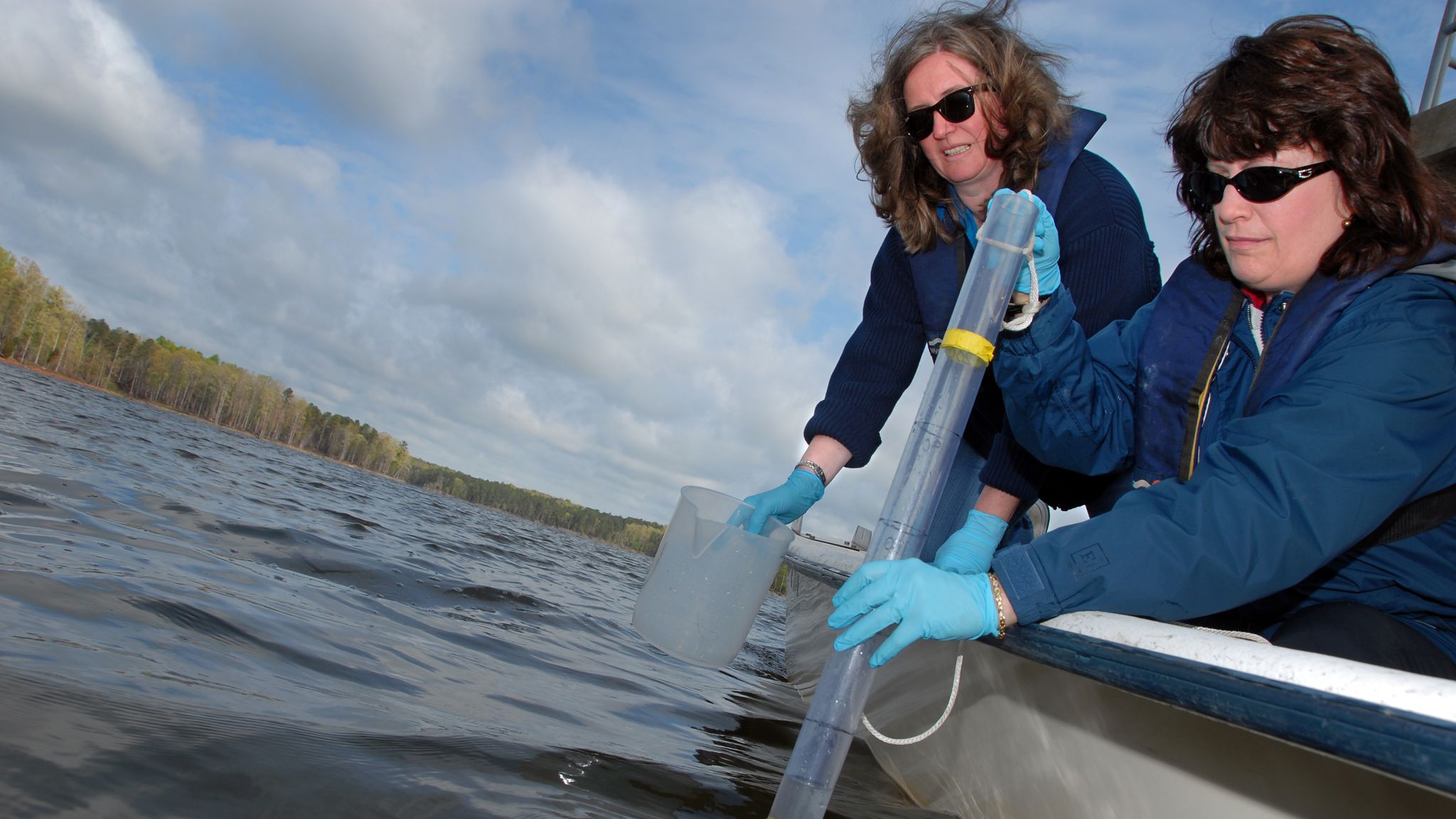 Two women out on a boat collecting a water sample.