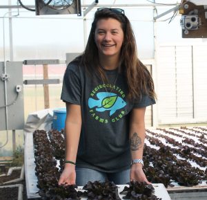 Student in greenhouse holding up a float bed with lettuce.
