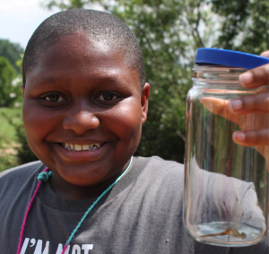 Middle school boy holding up a jar with an insect.