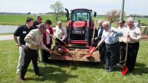 people shoveling dirt from front of a tractor at a ground-breaking event