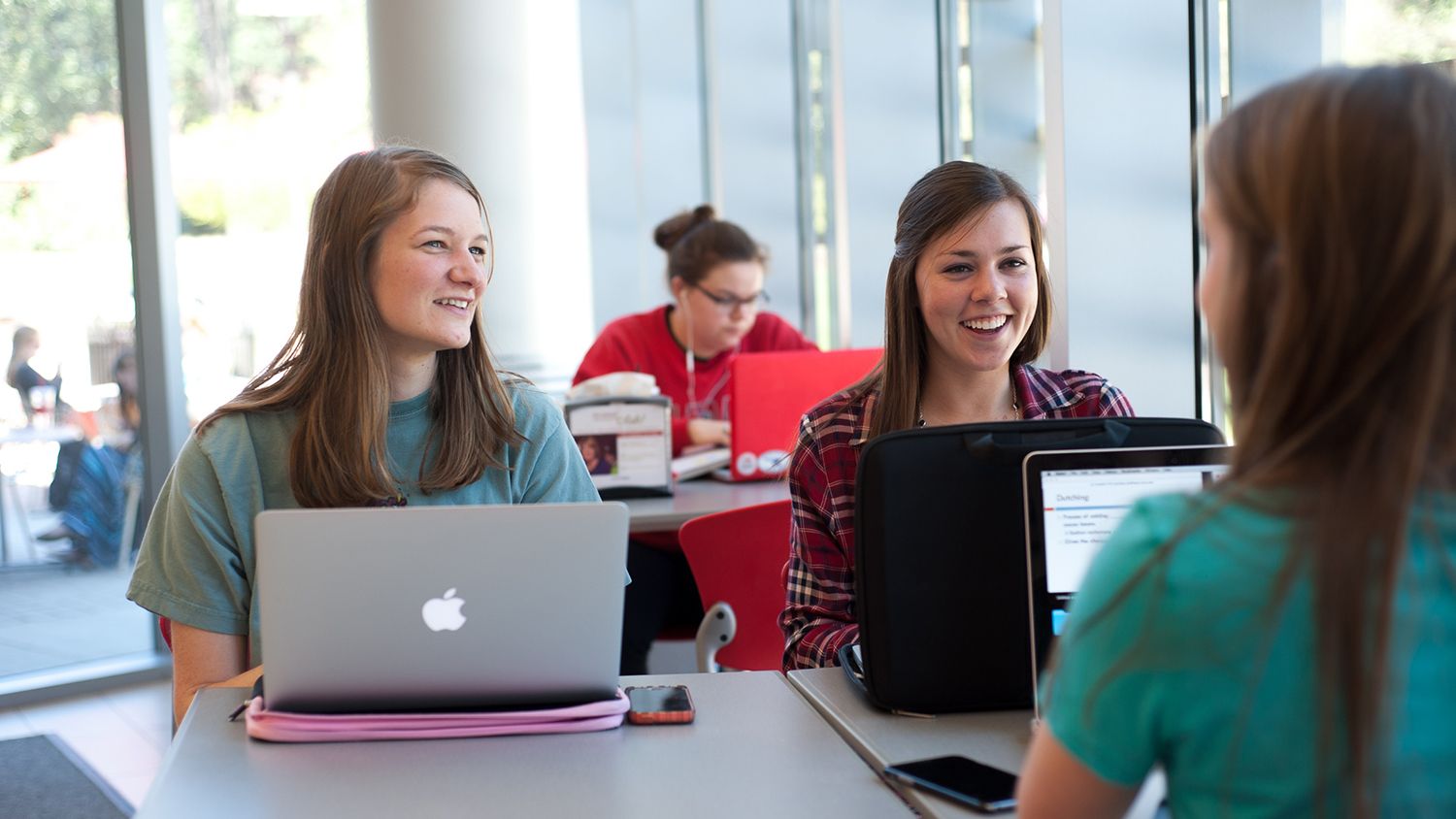 Three female students with laptops laughing in the library.