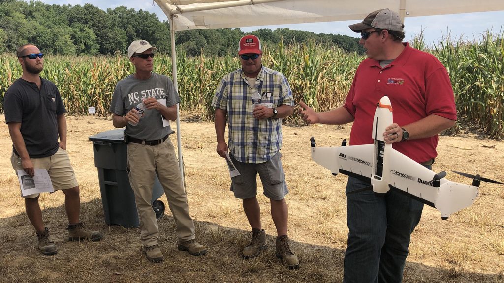 Four men under a canopy, one holding an unmanned aerial vehicle, or UAV