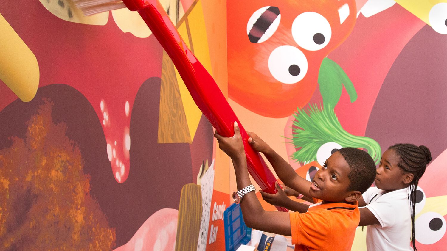 A boy and girl play with a giant toothbrush at an interactive oral health display.