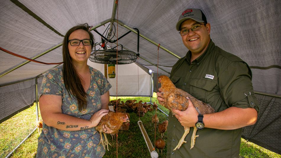 Man and woman holding chickens at their farm.