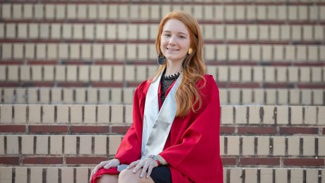 Woman in a graduation robe sitting on brick stairs