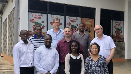 A group photo of nine individuals, African and Caucasian in front of a store front in Kenya.