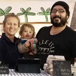 A man and a woman holding their child at a farmers market stand