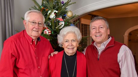 Bill Collins, Ann Collins, and Dean Richard Linton wearing red in front of a Christmas tree.